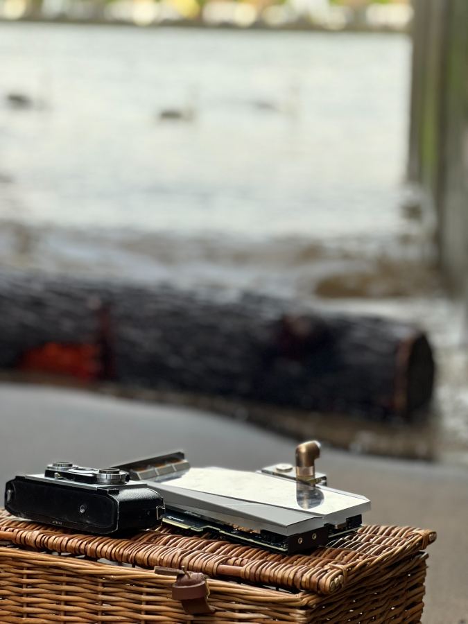 Film camera and hard drive on wicker basket, lake behind